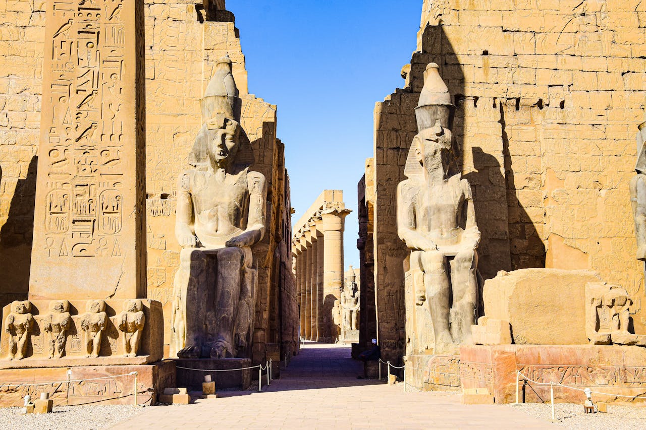 Entrance to Luxor Temple adorned with ancient Egyptian statues under clear sky.