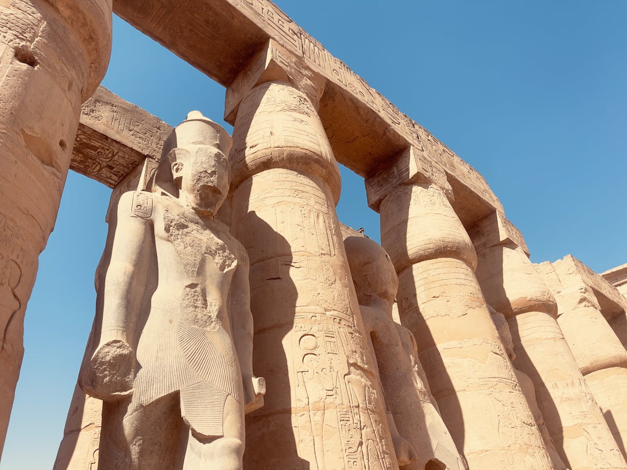 Majestic statues and columns at Luxor Temple under a clear blue sky.
