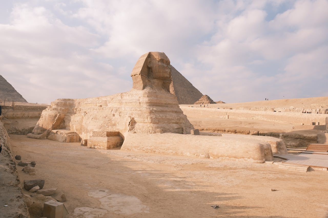 The Great Sphinx of Giza against a backdrop of pyramids and a partly cloudy sky.